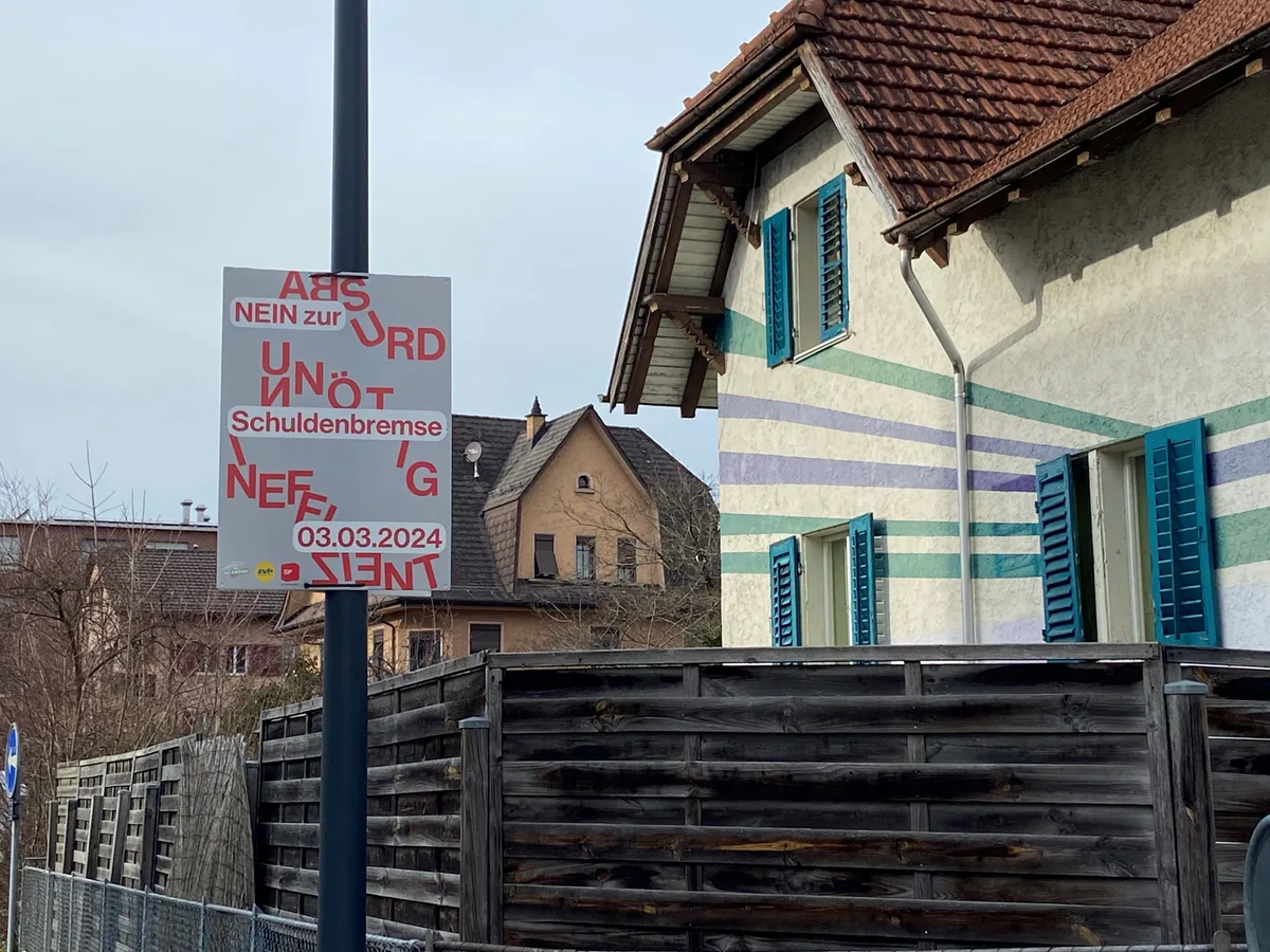 Plakat in Uster gegen die Schuldenbremse, steht neben einem kunterbunten Haus.